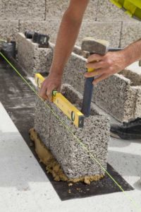 Construction worker building wall with Durisol checks to ensure bricks are level